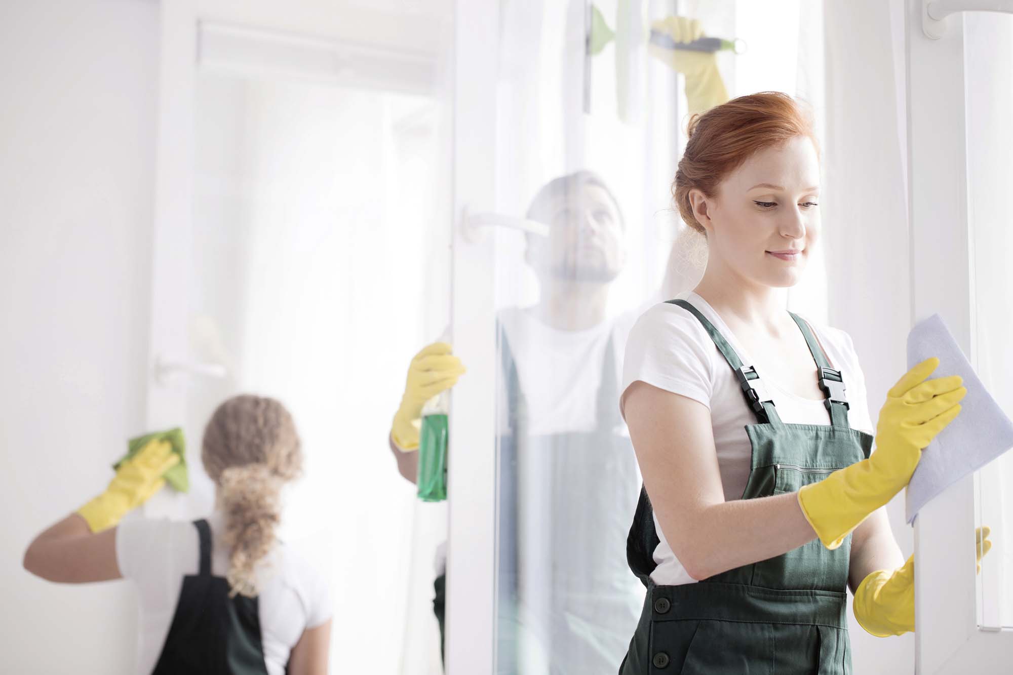 Young women in yellow gloves cleaning a window frame with her friends from cleaning service