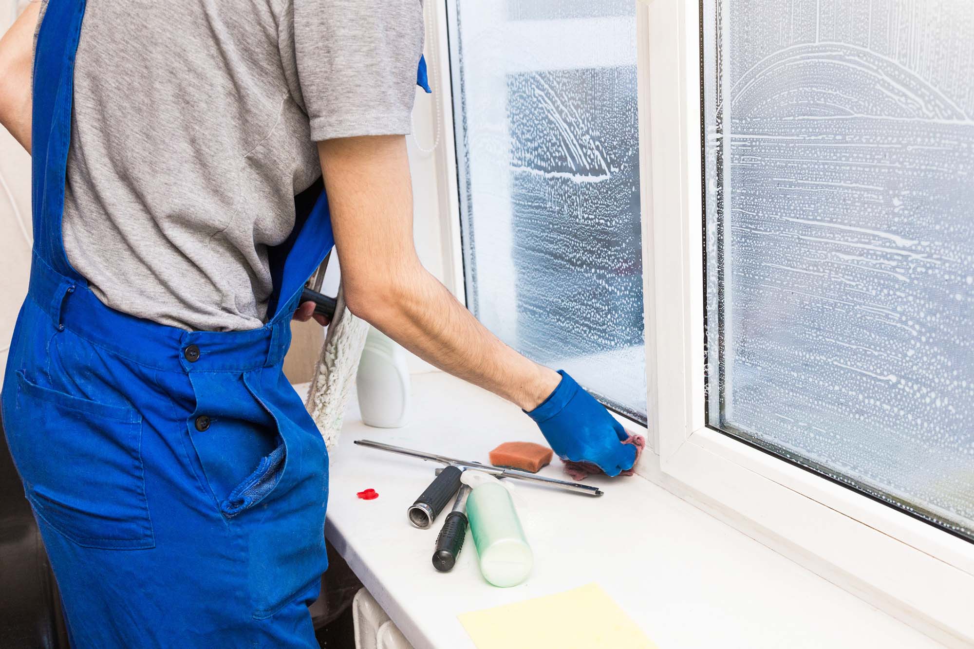 Close-up of a man in uniform and blue gloves washes a windows with window scraper. Professional home cleaning service.